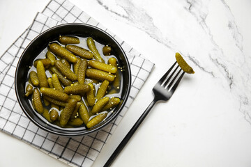 Bowl and fork with tasty pickled cucumbers on white background
