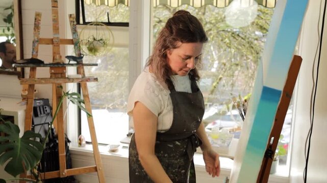 Painter puts canvas on easle, scenic studio, side view