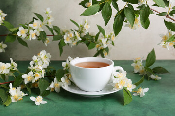 Cup of hot jasmine tea with flowers on green table