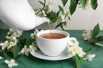 Pouring hot jasmine tea from teapot into cup and flowers on green table