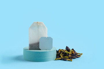 Composition with dry tea leaves, bag and plaster podium on blue background, closeup
