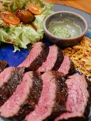Medium-rare steak slices served with crispy onions, leafy greens, and two dipping sauces at a fine steak restaurant in Bangkok, Thailand.