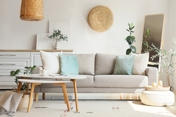 Interior of living room with comfortable sofa, pouf and tables near white wall