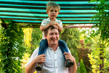 Close portrait of smiling dad giving ride beneath green striped pergola while his thoughtful...