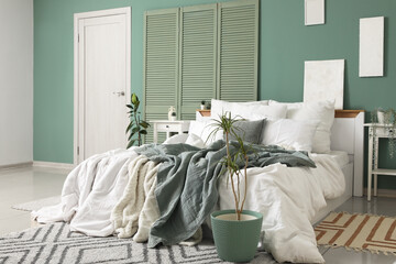 Big comfortable bed, folding screen and bedside table near green wall in interior of bedroom