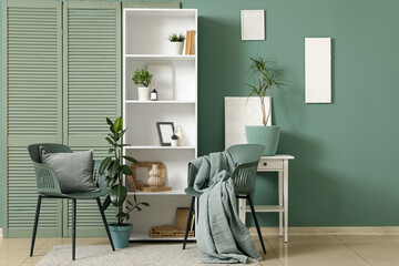 Shelving unit, folding screen and chairs near green wall in interior of modern room, closeup