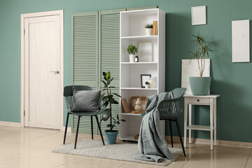 Fototapeta premium White door, shelving unit, folding screen and chairs near green wall in interior of modern room