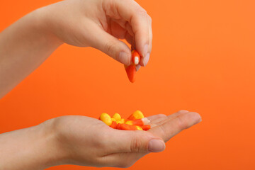 Female hands with chewy candies on orange background