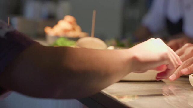 A restaurant pass lined with meals, ready and waiting to be taken to customers. A waiter steps in, lifts the plates and docket, and carries them away.