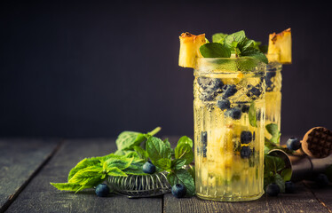 Refreshing mojito cocktail with pineapples and blueberry on the rustic background. Selective focus.
