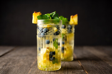 Refreshing mojito cocktail with pineapples and blueberry on the rustic background. Selective focus.
