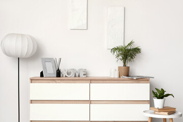 Chest of drawers, table and floor lamp near white wall in interior of room
