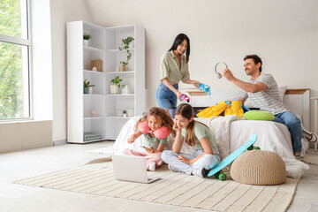 Family of tourists with laptop packing suitcase in bedroom