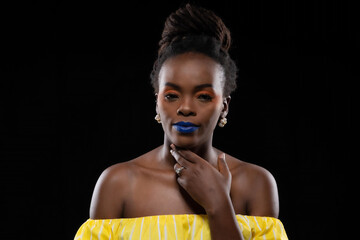 Close-up beautiful portrait black woman updo hairstyle showcasing creative makeup with blue lips and orange eyelid against at studio shot on black background.