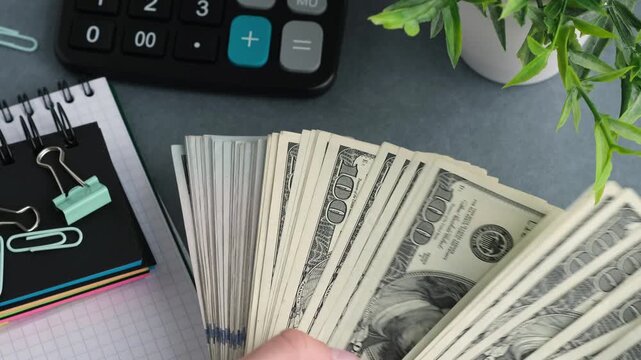 A stack of one thousand dollar bills on a desk. The stack is on top of a calculator and a stack of paper clips
