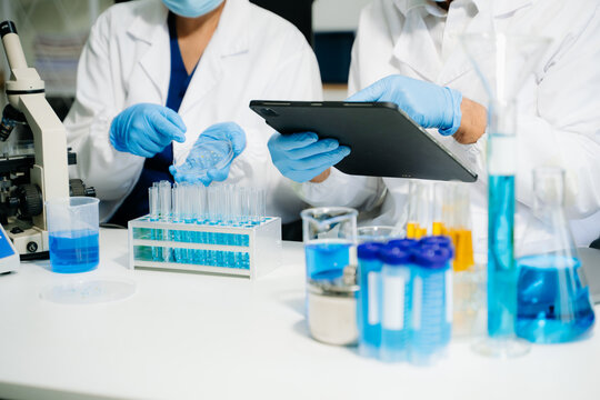 Scientists in a clean lab environment analyzing samples using test tubes and a tablet, showcasing modern biotech research, diagnostics, and medical innovation.
