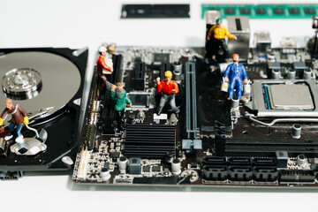 Creative tech concept showing miniature workers repairing an open hard disk drive on a motherboard....