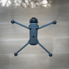Drone is positioned on a light wooden surface, capturing detailed shadows cast by leaves above. It's a bright midday, emphasizing the contrast in the scene.