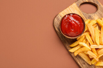 Wooden board with tasty french fries and bowl of ketchup on brown background