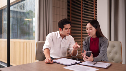 Asian business professionals collaboratively discuss strategies using smartphone and documents in a modern office meeting room