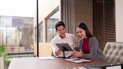 Asian Business Professionals Collaborating Reviewing Financial Data on Tablet and Smartphone in Modern Office