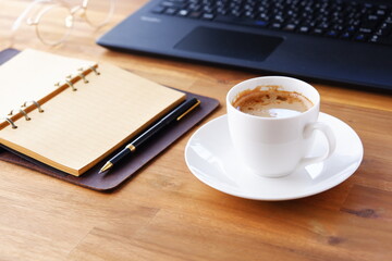 机にリング式のシステム手帳を広げ、淹れたてのコーヒー（カフェ・ラテ）を飲みながら、パソコンでデスクワークをしているイメージ
