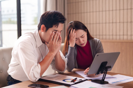 Asian business couple facing financial stress reviewing documents in office struggling with complex data analysis and challenging market conditions - Powered by Adobe