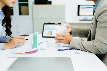 Two professionals analyze financial charts using digital devices in office.