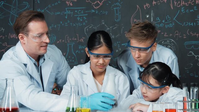 Smart teacher support and look after young diverse children doing experiment together. high school student with mixed races inspect biochemical liquid on table with microscope on table. Edification