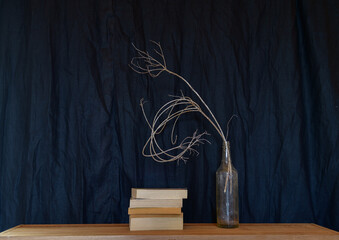 Vase with grasses and pile of books on black background