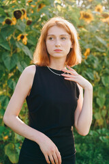 Elegant Young Woman with Red Hair in Black Dress and Necklace in Sunflower Field
