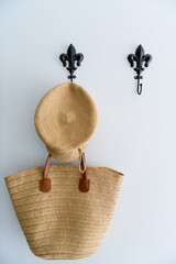 Hat and sea grass basket hanging up on vintage hooks on a white back ground