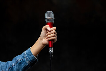 Hand of female singer wearing jeans holding a dynamic microphone isolated on black background.