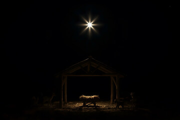 A dramatic nativity scene at night with an empty wooden manger in the center, softly lit by a single bright star shining