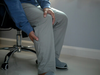 Businessman sitting on a chair for a long time until his knee hurts. Man's hands around his knee,...