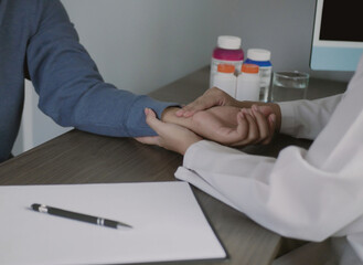 A female doctor is checking the pulse and heart rate of a patient in the hospital, fingers, and...