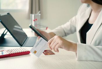 Beautiful Asian woman shopping online holding a credit card and using her smartphone to enter the...