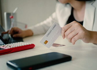 Beautiful Asian woman shopping online holding a credit card and using her smartphone to enter the...