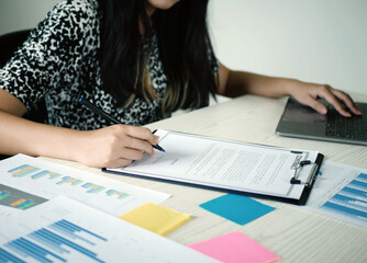 Young Asian business woman sitting at the table holding a pen, recording investments and planning...