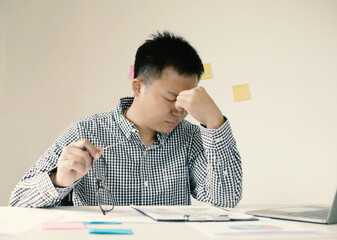 A young man office worker feels tired from migraines while working, is overworked, and stressed...