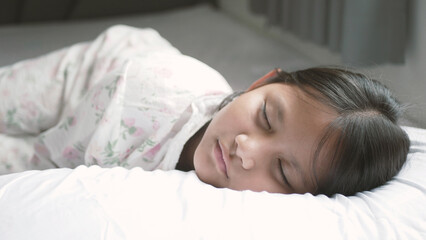 Obraz premium A girl is sleeping on a bed with plain white sheets in a bedroom at home. Cute close-up face Sleep deeply Sleep sweet dreams Sleep relax Cute little child