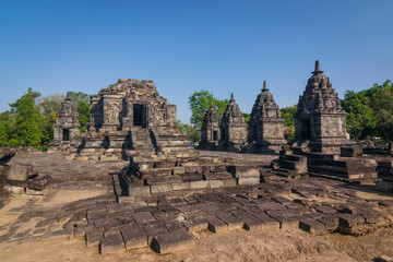 This wide-angle shot captures the ancient Candi Lumbung temple complex on Prambanan under a clear blue sky.