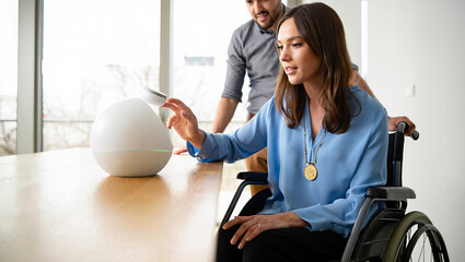 Woman in wheelchair using smart speaker with man assisting