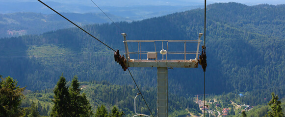 A mountain slope with a working chairlift, and behind it, a wide panorama of mountains covered with a dense forest. The image is ideal for illustrations on the theme of tourism, travel, nature, active