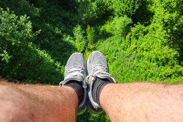 A pair of legs in sneakers dangle over a dense green forest, creating an exhilarating sense of height and adventure. The
