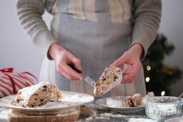 A person carefully cutting a festive holiday cake, dusted with powdered sugar, preparing to share a...