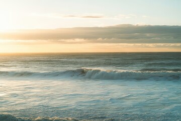 Obraz premium Sunlight reflects off gentle waves as the vibrant orange sky of a sunset paints the horizon over a sandy beach