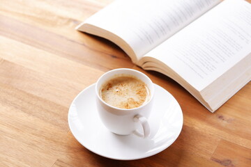 ページを開いたペーパーバック（洋書）とコーヒーの入ったコーヒーカップで、コーヒーを飲みながら読書を楽しんでいるイメージ
