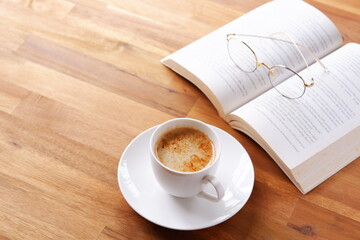 ページを開いたペーパーバック（洋書）とコーヒーの入ったコーヒーカップで、コーヒーを飲みながら読書を楽しんでいるイメージ
