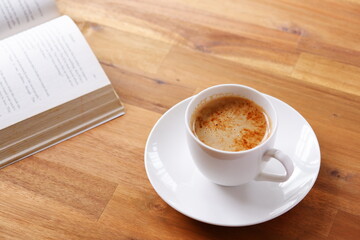 ページを開いたペーパーバック（洋書）とコーヒーの入ったコーヒーカップで、コーヒーを飲みながら読書を楽しんでいるイメージ
